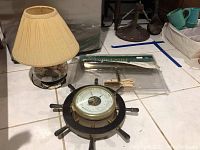 Overview of seashell lamp with beige pleated shade, Schatz ship wheel barometer, and packaged chrome picture light.