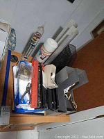 Photo showing assorted office supplies including paper ream, file organizers, hole punch, staplers, tape dispenser, plastic ruler, paper clips, and Galileo thermometer.