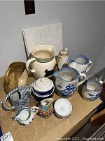 Overview of lot including various ceramic pitchers, covered sugar bowl, swan-shaped vase, small decorative pitchers, and three ceramic tiles stacked behind.