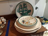 Photo of plates stacked showing ship-themed and musical decorative plates on top of solid white plates