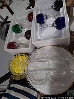 Photo of colored stemware glasses packed in white foam containers alongside yellow and white enamel pans.