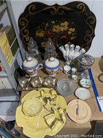 Overall assortment of items including large black serving tray, glass trees, ceramic jars, yellow leaf platter, metal condiment set, decorative plate, and various small ceramic and glass items.