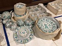Overall view of multiple hand painted Italian pottery items including plates, teapot, cups, creamers, sugar pot, oil and vinegar containers packed partially in padded holders
