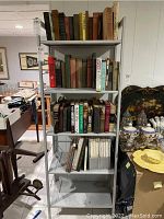 Gray five-tier metal shelf with multiple shelves of books in a basement setting