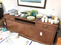 Sideboard from front, showing drawers, sliding doors, and condition of wood finish with various dishware on top (not included).