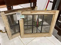 Two stained glass window panels leaning against furniture, showing full front view and skins of frames with visible wear and dirt.