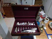 Open wooden chest lined with burgundy fabric showing flatware contents