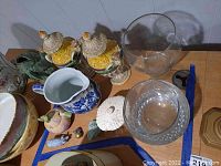 Wide grouping showing vases, pitcher, glass bowls, lidded boxes and small figurines on wood surface