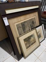 Five stacked framed prints leaning against a wall, showing varying frame styles and visible parts of the prints including architectural arches and outdoor scenes.