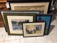Five pieces of framed wall art stacked on the floor showing varying landscape and animal themes.