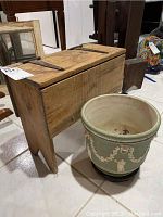 Photo showing wooden Wedgewood chest, rustic with metal hinges, alongside pale green ceramic planter vase on white tile floor.