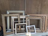 Photo showing eight assorted art frames standing against a brown fabric background, highlighting different sizes, styles, and finishes including gilted and natural wood