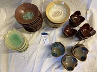Photo showing stacks of tan and brown fish-shaped bowls, light green fish-shaped plates, and brown and blue condiment dishes arranged on fabric.