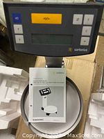 Top view of electronic paint mixing scale showing the keypad, display unit, and stainless steel pan with user manual beside it.