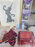 Overview of lot showing all items: framed Thai temple rubbing, two alpaca chullo hats, metal cylinder box, elephant hanging, agate art piece, ceramic figurine, and small ethnic mat.