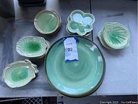 Overview photo showing large green glaze round dinner plates with small flower, lobster, and shell shaped side dishes around.