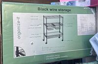 Box of black wire 3-tier shelving unit with 2 sliding baskets on wheels, showing detailed specs and product image on box