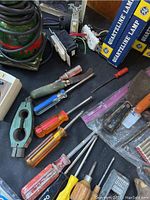 Photo showing an assortment of screwdriver handles in various colors and a metal hand tool accessory, along with boxed quartzline lamps on a black surface.