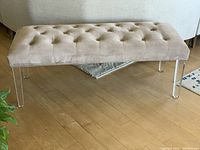 Close-up side view of the light grey tufted bench with clear Lucite-style legs on hardwood floor.