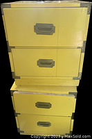 Two stacked yellow wooden campaign style nightstands with metal corner brackets and drawers with recessed handles.