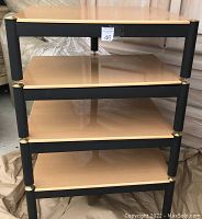 Four-level stereo stand stacked with glossy gold rectangular shelves and black metal supports with brass accent caps.