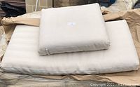 Photo of two off-white chaise lounge cushion pads stacked with the smaller backrest cushion on top of the larger bottom pad. Cushions have neat rectangular shapes and appear firm with a spa-like look.