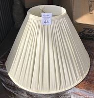 Front view of classic linen pleated lamp shade showing pale white fabric and wide flared shape.