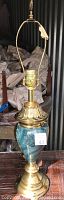 Full lamp view showing brass base, faux teal marble mid-section, brass harp and socket with power cord attached.