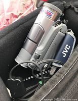 Close-up of silver JVC handheld video camera with 6x 680k pixel CCD in black carrying case, with attached cables visible.
