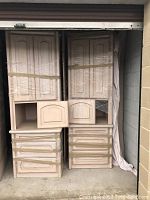 White ash headboard with left and right storage units wrapped for transport, showing cabinet doors and multiple drawers in natural wood finish.