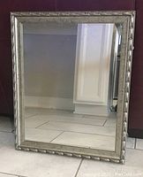 Front view of rectangular portrait mirror with antique style gold-painted carved frame, showing reflection of floor and wall.