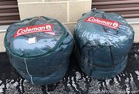 Two Coleman down sleeping bags packed in individual green compression sacks with clear top displaying Coleman logo.