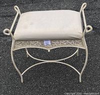 Photo showing one white metal stool with padded white moire fabric seat and decorative cast aluminum base on outdoor blacktop.