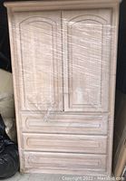 Photo of one wrapped tall white ash stained oak armoire showing paneled doors and three drawers underneath.