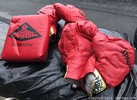 Two pairs of red Spalding boxing gloves placed next to a red Century handheld punch target, all lying on a black surface outdoors.