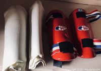 Photo showing two white fabric shin guards and two red forearm elbow protectors with elastic and Velcro straps, all size medium for Tae Kwon Do.