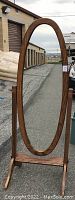 Front view of the full length oval mirror in walnut stained oak frame outdoors.