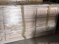 Photo of the oak dresser wrapped in plastic showing three stacks of three drawers each and white ash stained finish.