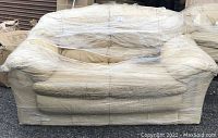 Yellow leather loveseat wrapped in plastic showing front and side arms.