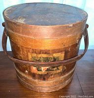 Full view of the firkin showing its round wooden body, handle, and scenic paper label on the side