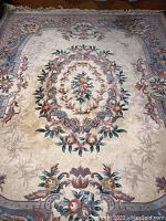 Photo showing the full 8x10 wool rug with cream background and multicolor floral center medallion and border.