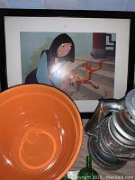 Disney wall art partially visible in frame behind orange mixing bowl and metal lantern. Items arranged on table.