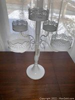 Front side view of the five arm white metal candleholder showing ornate decorative detailing on candle plates and round base.