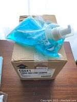 Plastic bag with blue foaming shampoo and pump on top of the original cardboard box.