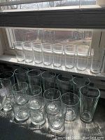 Set of 24 ribbed clear glass drinking glasses arranged in groups by size, with 8 tall glasses on the back row, 8 medium glasses in front, and 8 short glasses at the front side.