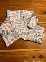 Two natural rice filled heating pads with colorful gem patterns lying on wooden surface, showing overall design and tags attached.