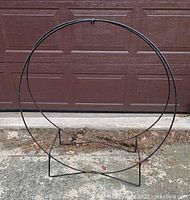 Front view of black metal circular firewood holder standing upright on concrete surface outdoors.
