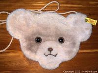 Front view of plush teddy bear face coin purse showing button eyes, embroidered nose and mouth, and Steiff tag on ear.