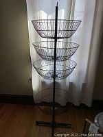 Full view of tall metal storage stand with four wire baskets stacked vertically and spinning around central pole.