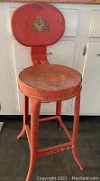 Full view of red metal stool showing original paint and signs of wear and rust